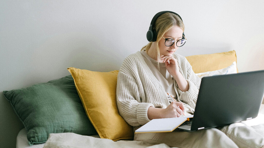A free to use image from Pexels, taken by photographer Ivan Samkov, showing a woman working on a laptop while wearing headphones