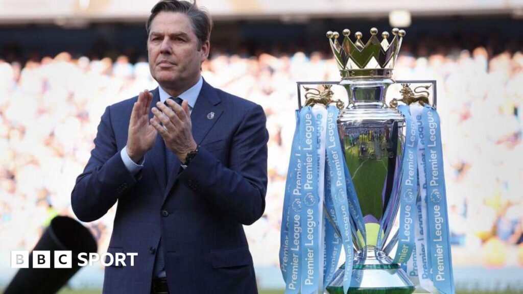 Richard Masters standing next to the Premier League trophy, which is in Manchester City colours
