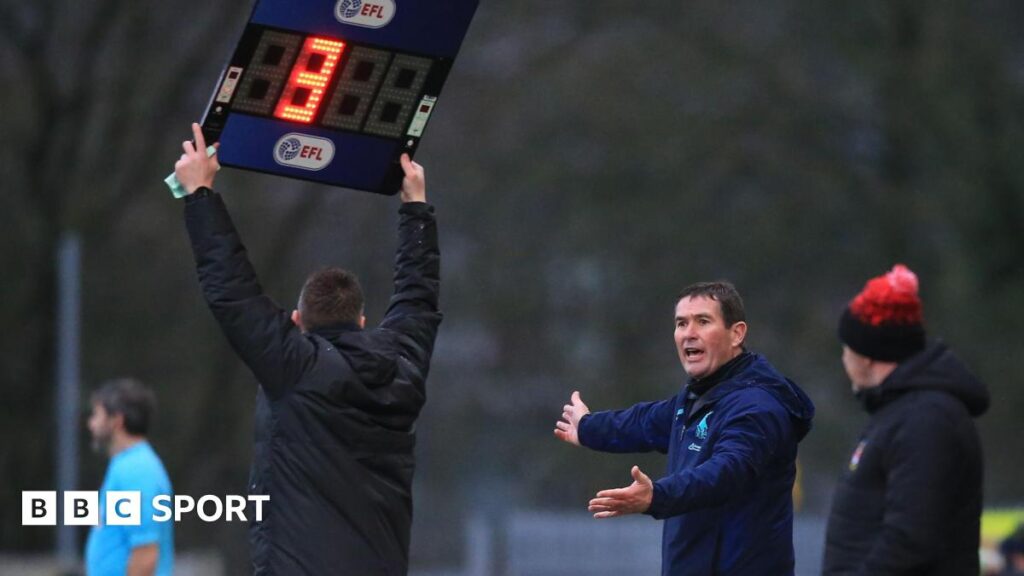 Mansfield boss Nigel Clough talking to a fourth official as he hold up a board to indicate how many additional minutes are to be played