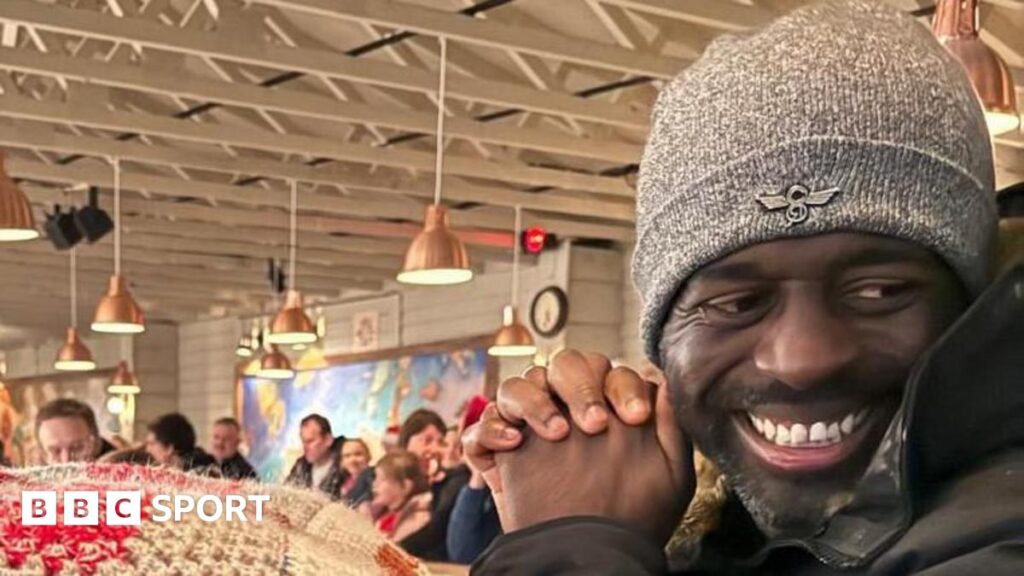 Marvin Brown: Former Bristol City forward dies aged 42 from cancer Man in grey hat with black beard smiling off to the side with a busy bar or pub setting behind him.