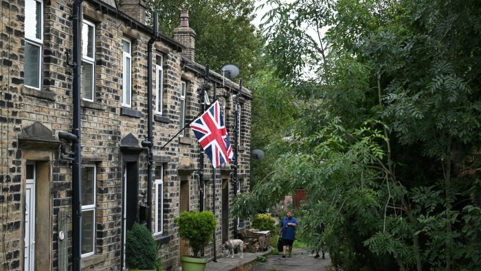 Why local democracy must not flag A Union flag flies from a pole on the front of a terrace house in Slaithwaite, with a person and a dog visible on the path.