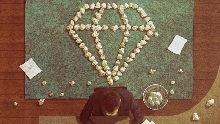 Creativity thrives with constraints A man sits at a work desk with crumpled sheets of paper on the floor. An array of paper balls have been formed into a diamond shape on the floor behind him.
